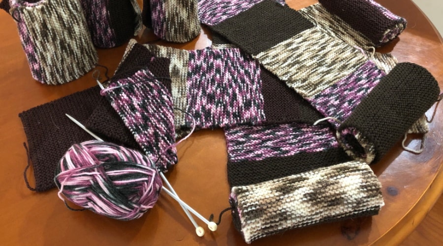 Knitting needles with work in progress and rolls of rows of already knitted blanket