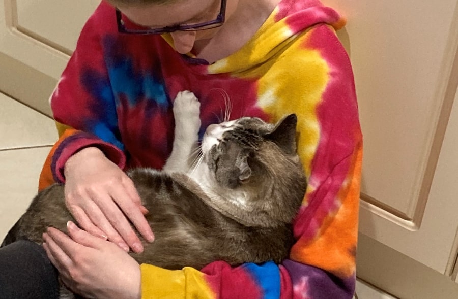 Lady in tie dyed hoodie cradling a sleeping cat.